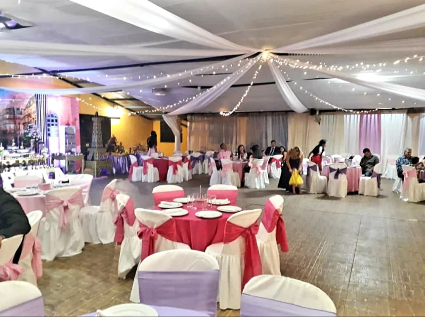 El salón con el techo vestido de tela blanca y luces, y mesas con manteles rosa